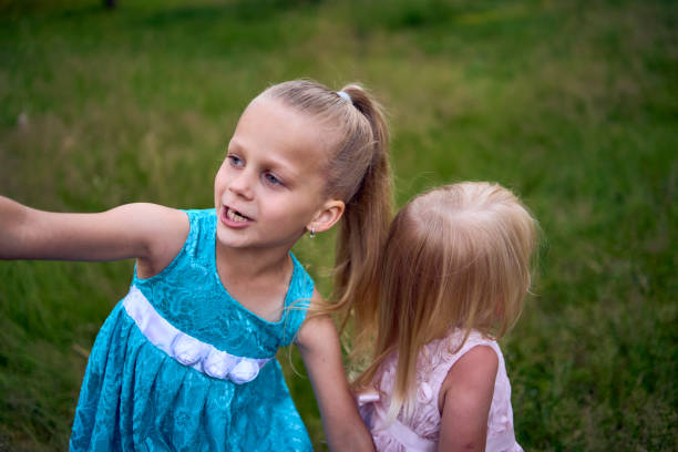 two little sisters in dresses playing together in the tall grass