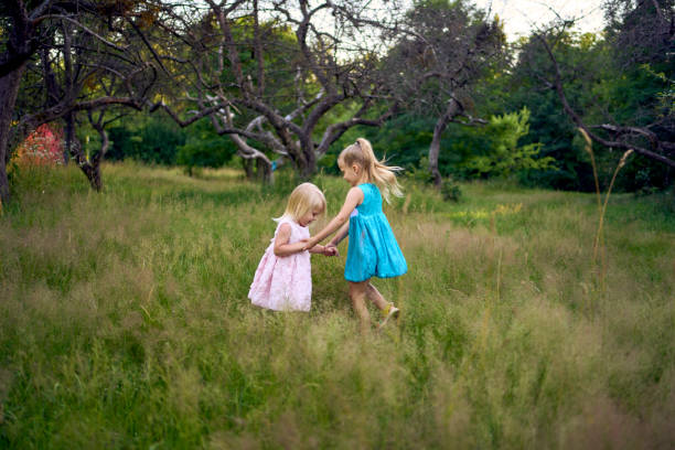 two little sisters in dresses playing together in the tall grass