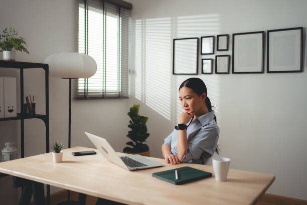 istock Asian woman sitting at home office, feels concerned thinking about work. 2159178218