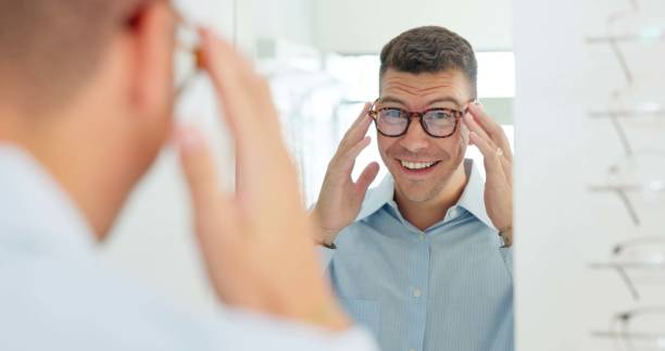istock Man, glasses and mirror at store for optometry, vision or wellness for eyesight, smile and choice. Person, customer and check reflection with decision for eye health, happy and style at retail shop 2159182932