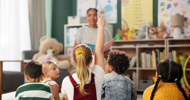istock Kindergarten, children and question for teacher in class at montessori school, learning and reading story. Kids, fairytale and woman teach girl with creative ideas or talking in preschool education 2159187471