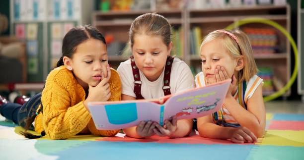 istock Children, book and reading together at school, learning and literacy knowledge or mind development. Girls, kids and storytelling for education, english and literature information on mat for language 2159187475