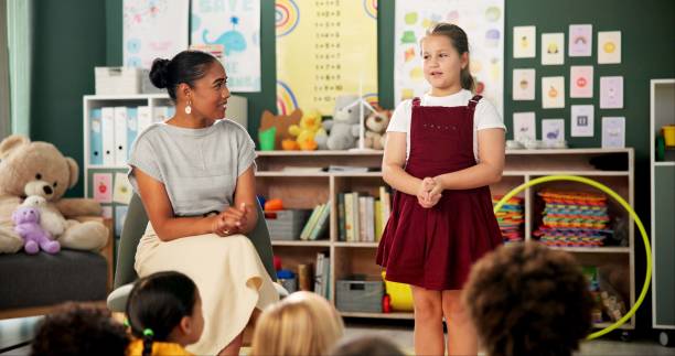 istock Classroom, education and teacher with kid student or presentation, teaching and public speaking support. Learning, school or woman with girl for speech, help or guide to self confidence development 2159187485