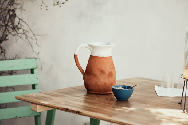 White and Terracotta Ceramic Pitcher on a Wooden Table Top in a Leafy Shadow
