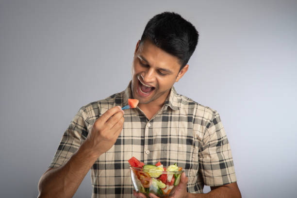 istock Man smiling and eating fruit salad on gray background 2159190016
