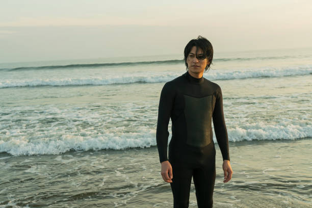 Surfer man in wetsuit stretching arms on a sandy beach, preparing for surfing amidst lush green tropical jungle