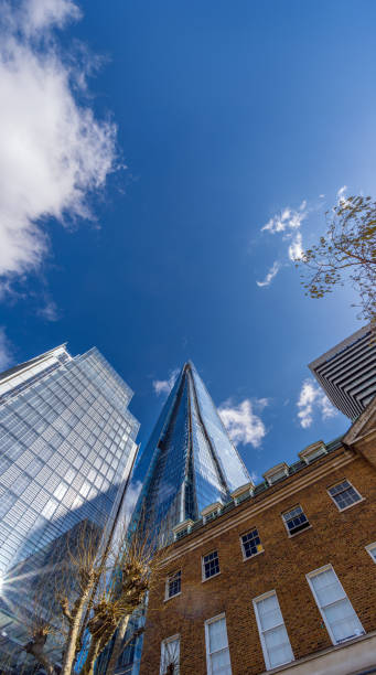 Low angle view of modern pyramid shaped glass skyscraper The Shard with blue sky and some clouds reflected in the buildings windows with reflected sun rays. London. United Kingdom.