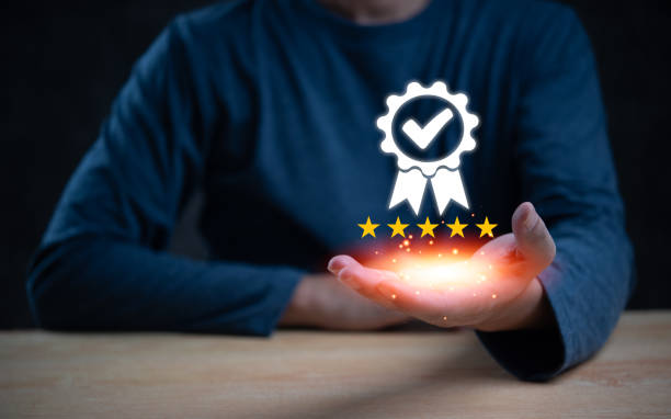 istock Hand holding a glowing five-star quality assurance badge with a checkmark. Represents excellence and certification. Perfect for quality control, customer satisfaction, and service standards. 2159200187