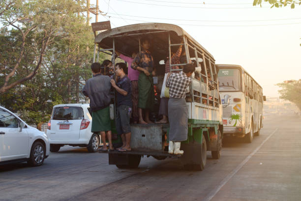 03/12/2018 - Yangon, Myanmar: Busy street scene in Yangon, Myanmar, showing a packed local transport vehicle with passengers boarding and hanging onto the sides, capturing the bustling urban life and transportation challenges in the city.