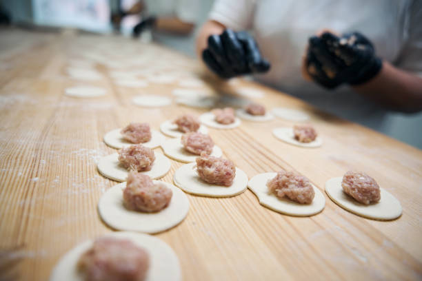 Kitchen worker lays out pieces of minced meat on blanks for dumplings, a woman works on a wooden surface