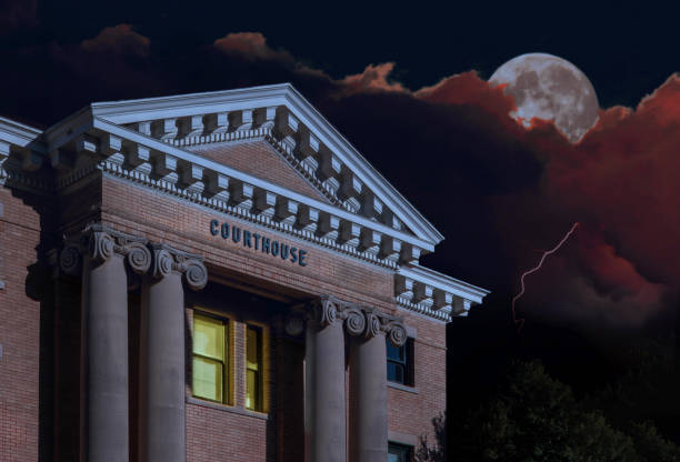 Lights on in a courthouse office at night making a deal with a lightning storm behind and the moon rising.