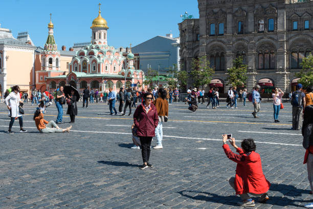 Portrait of serene adult caucasian woman in grey jacket and hat standing on city street in a cold cloudy day in Moscow. Blurred Saint Basil's Cathedral and illuminated street light in the background.
