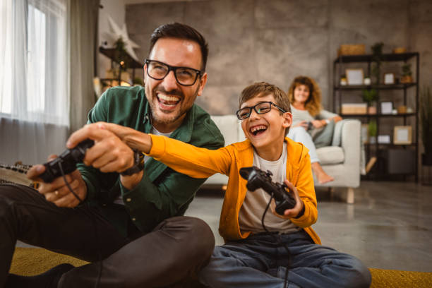 istock Dad and son play video games with joystick while mum wife watch them 2159238499