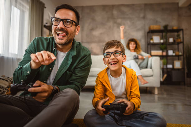 istock Dad and son play video games with joystick while mum wife watch them 2159238563