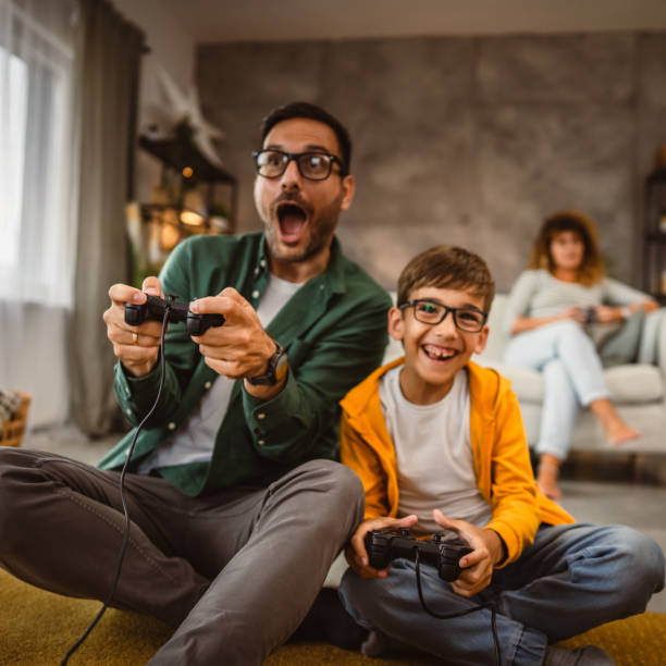 istock Dad and son play video games with joystick while mum wife watch them 2159238592