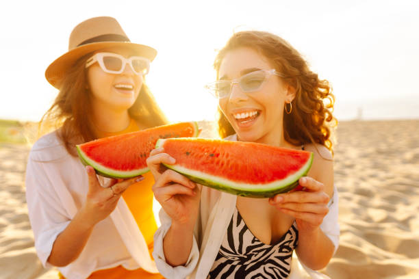 istock Two laughing women with watermelon on beach. 2159241171