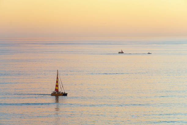 A sailboat peacefully floats on the calm surface of a lake, while the sky above is painted with the hues of dusk, creating a serene atmosphere