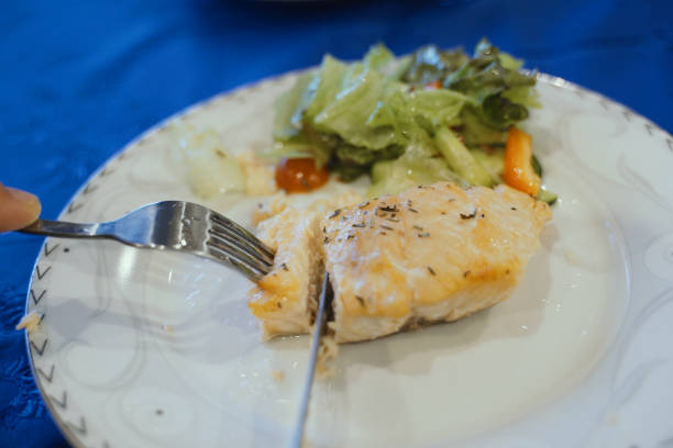 A piece of grilled salmon seasoned with herbs on a white plate accompanied by a fresh green salad, ready for a healthy meal.