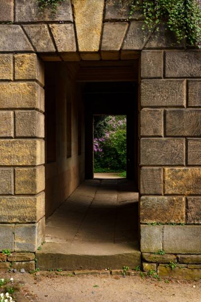 istock Stone passageway with large rectangular blocks forming the walls and doorway with garden view. Stonework as architectural detail with perspective view. Historic construction from weathered stone 2159256051
