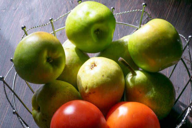 Green apples and red tomatos on a metal basket , on the table