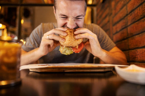 istock A hungry man sitting in restaurant and biting delicious hamburger. 2159293713