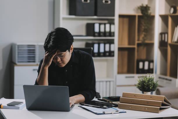 istock Frustrated Asian young businessman worker working on table in office. Busy employee worker people feel tired and headache from late work and overwork job document on computer desk at company workplace 2159294295