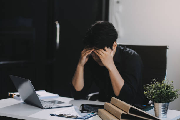 istock Frustrated Asian young businessman worker working on table in office. Busy employee worker people feel tired and headache from late work and overwork job document on computer desk at company workplace 2159294298