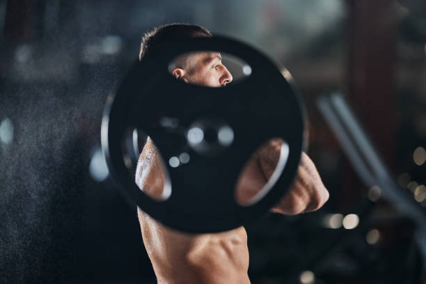 Determined sportsman exercising with barbell in a gym.