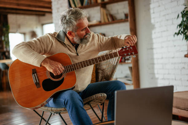 Mature man tuning an acoustic guitar at home.