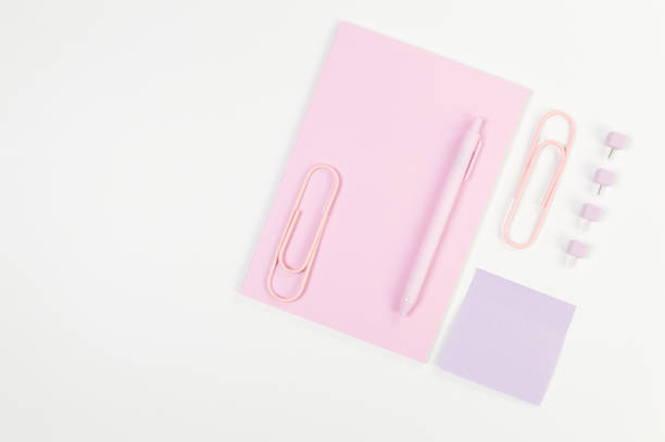 istock Top view of pink notebook on white background. Sticky note, paperclips, pen and pins. School, office wallpaper. 2159306845