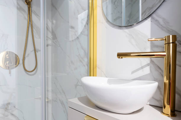 istock Home interior with ceramic bathroom sink on cupboard with gold water tap and shower with tile on the wall with marbled effect.  Interior decor. 2159313508