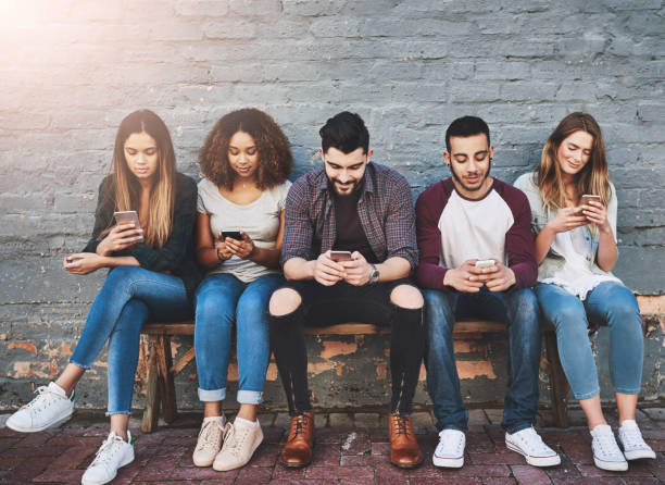 istock Students, row and outdoor with smartphone on bench for study break, social media and campus friends. University, people and online with technology for communication, wall background and relax 2159314461