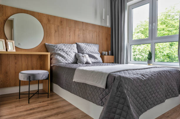 Modern bedroom with double bed, parquet floor and window with curtain. Home interior. Simplicity in architecture and decoration and design. Relaxation and comfort zone.