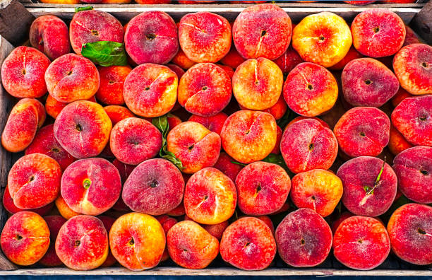Saturn peaches arranged in a wooden crate at a market.