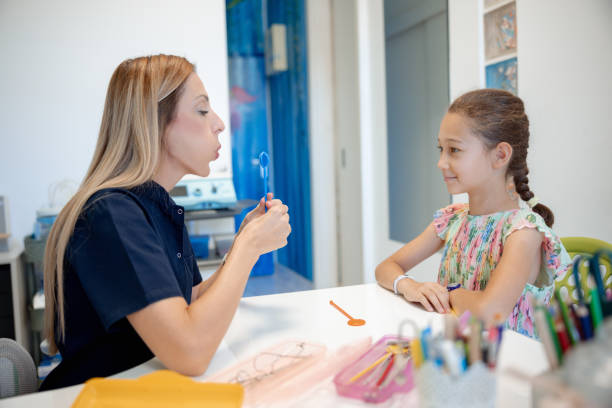 istock Female speech therapist showing elementary age girl how to use special tool at speech therapy 2159323954