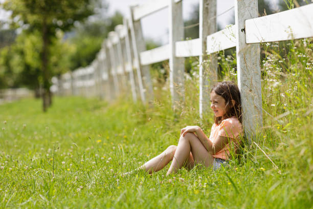 Child sitting in grass and leaning on ranch fence. Enjoying the day.