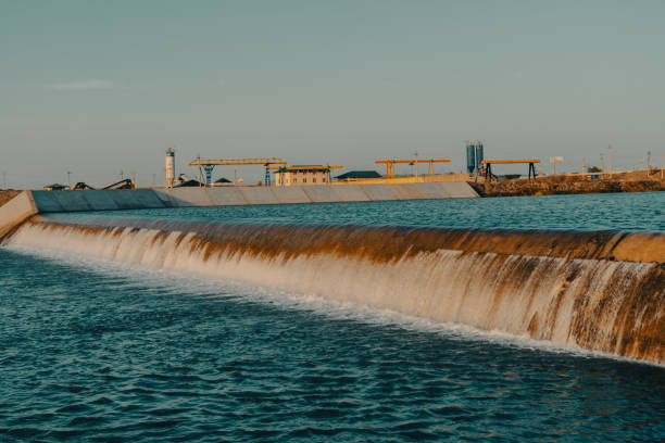 A long waterway with a waterfall and a building in the background. The water is calm and clear