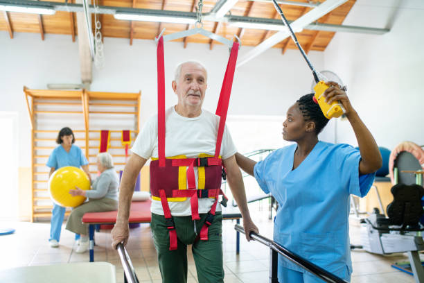 istock Elderly man with straps walking between the parallel bars with help from therapist 2159332051