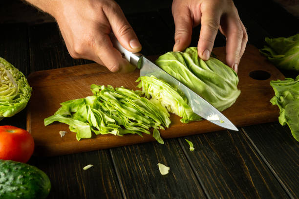 istock Chefs hands with a knife cut fresh cabbage on a kitchen board to prepare a vegetable salad for lunch at the hotel. Advertising space 2159334352
