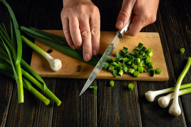 Chef hands using a knife to cut green garlic on a cutting board for preparing a vegetarian dish or salad. Place for advertising