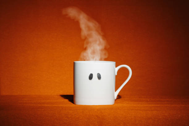 White mug with sparkly spooky ghost eyes and hot steam on orange background. Creative minimalist Halloween wallpaper