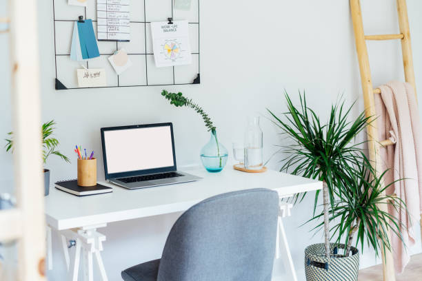istock Modern Contemporary workplace design. White desk with laptop mockup empty screen, grid mood board with pinned notes and plans, green plants, office supplies at work space in home office room interior 2159348817
