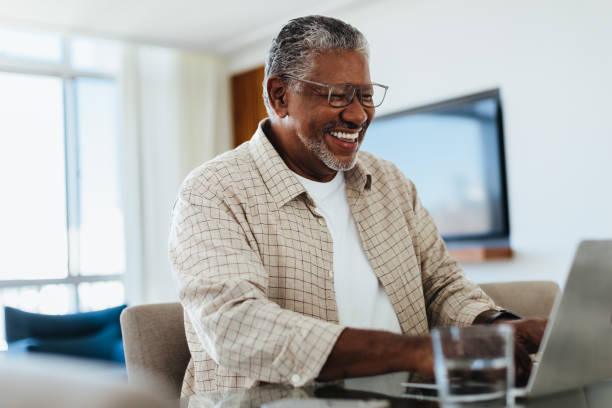Happy senior man using laptop at home, enjoying technology