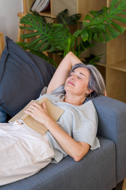 istock Senior woman falling asleep while reading on sofa at home 2159351264