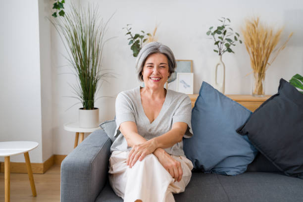 istock Senior woman smiling while relaxing on sofa at home 2159352092