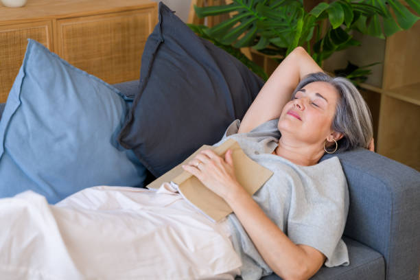 istock Senior woman sleeping peacefully on sofa after reading a book at home 2159352429