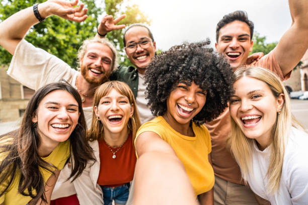 des amis multiculturels souriant à la caméra ensemble à l’extérieur - des jeunes heureux prenant un selfie avec un téléphone portable intelligent marchant dans la rue de la ville - communauté de jeunes et concept technologique - groupe de personnes photos et images de collection
