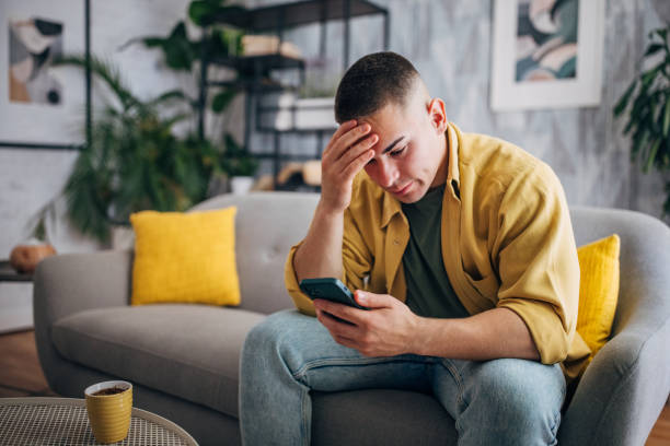 Stressed Man with smartphone and coffee cup An individual is looking worried while browsing his smartphone , seated with a coffee cup on the table in a peaceful home setting edgy man stock pictures, royalty-free photos & images