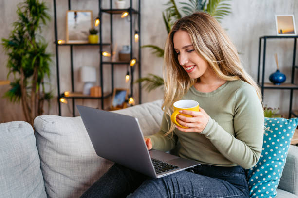 istock Young Woman Drinking Coffee And Working On A Laptop While Sitting On The Sofa At Home 2159356036