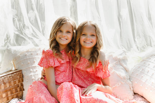 Beautiful, identical twin girls, nine years old, in a garden. Lace curtains in back ground.